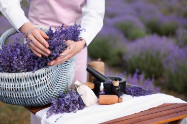 Doğal kozmetik ürünleri yapıyorum. Hasır sepet lavanta çiçekli bir kadın ve diğer malzemeler masada, yakın plan. Metin için boşluk