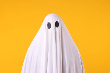Ürkütücü hayalet. Turuncu arka planda beyaz çarşaflı bir adam.