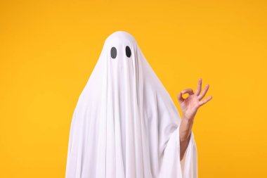 Hayalet kostümlü adam turuncu arka planda iyi niyet gösterisi yapıyor.