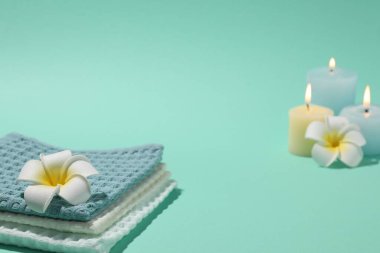 Katlanmış waffle havluları, tesisat çiçekleri ve turkuaz arka planda yanan mumlar, yakın plan.