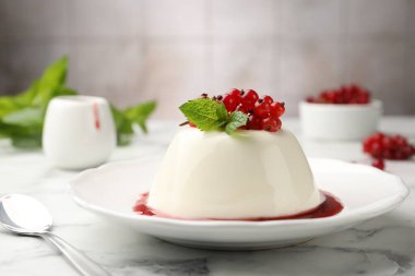 Kırmızı üzümlü, soslu ve naneli nefis panna cotta beyaz mermer masada bulanık arka planda, yakın planda