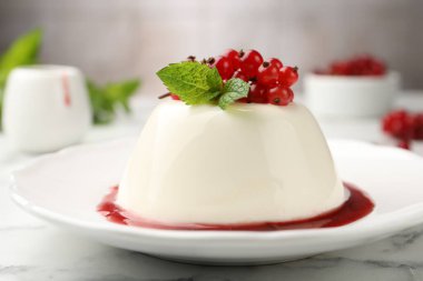 Kırmızı üzümlü, soslu ve naneli nefis panna cotta beyaz mermer masada bulanık arka planda, yakın planda