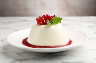 Kırmızı üzümlü, soslu ve naneli nefis panna cotta beyaz mermer masada bulanık arka planda, yakın planda