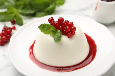 Kırmızı üzümlü lezzetli panna cotta, beyaz mermer masada sos ve nane, yakın plan.