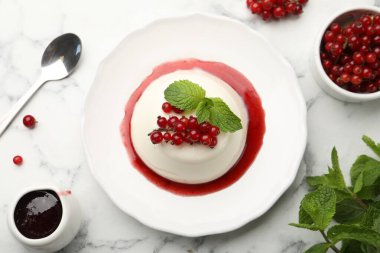 Kırmızı üzümlü lezzetli panna cotta, beyaz mermer masa üzerinde sos ve nane, düz yatıyordu.