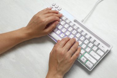 RGB ışıklandırmalı modern klavyede yazan kadın beyaz ahşap masa, üst görünüm