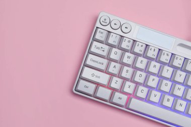 Pembe arka planda RGB ışıklandırmalı beyaz klavye, üst manzara. Metin için boşluk