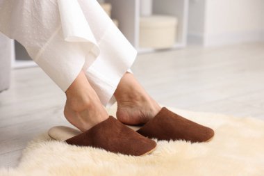 Yumuşak kahverengi terlikli bir kadın, yumuşak halıda, yakın plan.