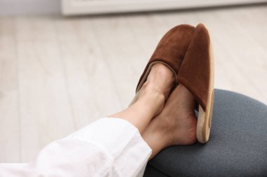 Yumuşak kahverengi terlikli kadın evde pouf 'un üstünde, yakın plan.