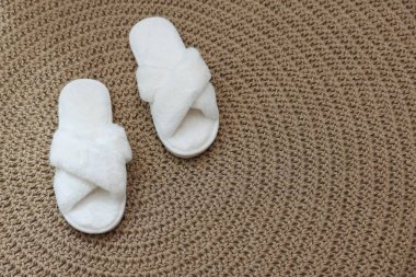 Hasır üzerinde tüylü beyaz terlikler, üst manzara.