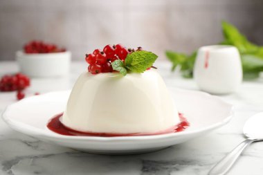 Kırmızı üzümlü, soslu ve naneli nefis panna cotta beyaz mermer masada bulanık arka planda, yakın planda