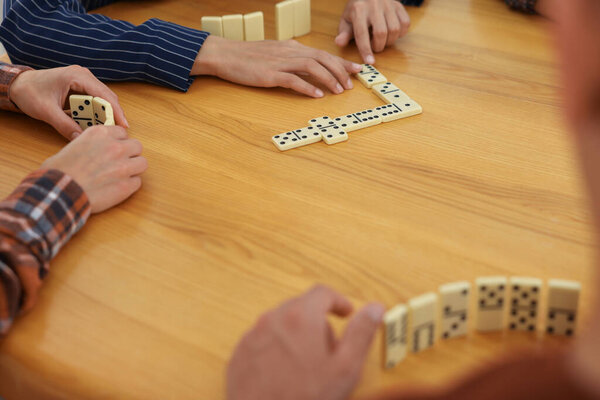 Друзья играют в домино за деревянным столом, крупным планом