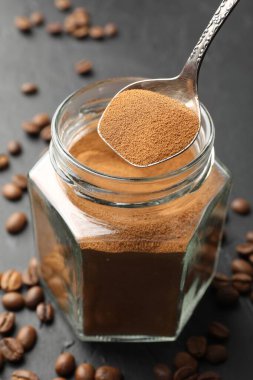 Kavanozdan siyah masada kaşıkla hazır kahve tozu almak, yakın plan.