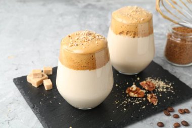 Bardakta lezzetli dalgona kahvesi, esmer şeker, fasulye, ceviz ve granüller gri masada, yakın plan.