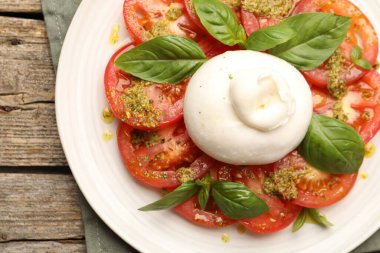 Ahşap masada mozarella, domates, fesleğen ve pesto soslu Caprese salatası.