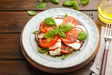 Mozarella, domates, fesleğen ve baharatlarla ahşap masaya yakın plan Caprese salatası.
