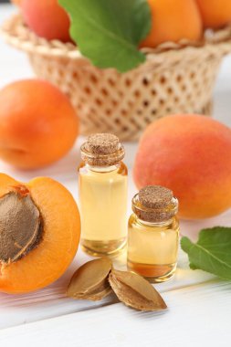 Beyaz ahşap masa üzerinde gerekli yağ şişeleri, taze kayısılar ve çekirdekler, yakın plan.