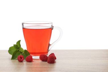 Lezzetli ahududu çayı, böğürtlen ve yapraklar beyaz arka plana karşı ahşap masada.