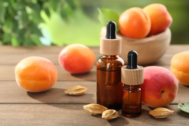 Şişelerdeki, tohumlardaki ve olgun kayısılardaki yağlar ahşap masada bulanık yeşil arka planda, yakın planda.