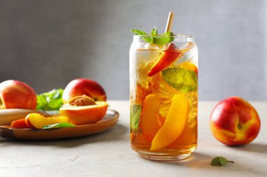 Buzlu şeftali çayı, bardakta nane şekeri ve beyaz masada taze meyveler, yakın plan.