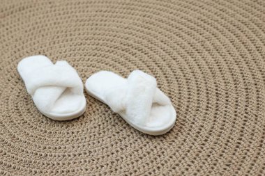 Hasır üzerinde tüylü beyaz terlikler, yakın plan.