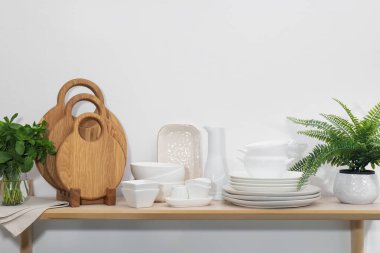 Temiz bulaşık takımı, kesim tahtaları, nane ve bitki beyaz duvarın yanındaki ahşap masada.