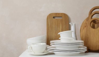 Mutfaktaki tezgahta farklı beyaz bulaşık takımları ve tahta kesme tahtaları var.