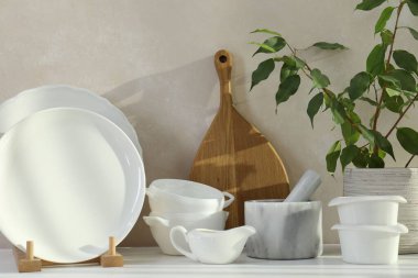 Farklı beyaz bulaşık takımı, ahşap kesim tahtası ve mutfak tezgahında ev bitkisi.