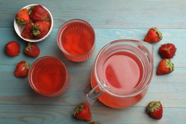 Bardaklar içinde lezzetli bir karışım, sürahi ve taze çilekler açık mavi ahşap masa üzerinde, düz uzanmış