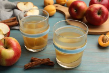 Bardaklarda lezzetli bir karışım, taze elmalar, kayısılar ve tarçınlı açık mavi ahşap masa, yakın plan