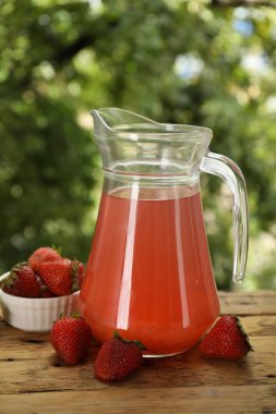 Cam sürahide lezzetli bir karışım ve açık havada ahşap masada taze çilekler.