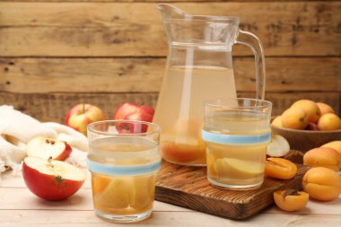 Bardaklar, sürahiler, taze kayısılar ve elmalar ahşap masada, yakın plan.