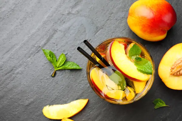 Buzlu şeftali çayı bardakta ve taze meyveler koyu masada, düz yerde. Metin için boşluk