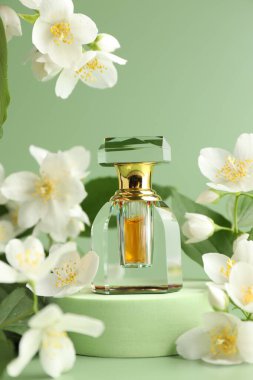Yeşil arka planda bir şişe parfüm ve yasemin çiçeği, yakın plan.
