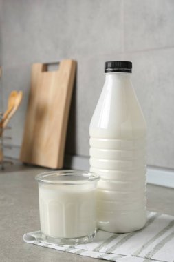 Süt ürünleri. Bardaktaki taze süt ve içerideki gri dokulu masada duran şişe.