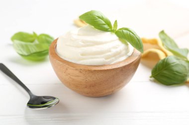 Lezzetli yoğurt, fesleğen ve kaşık beyaz ahşap masada, yakın plan.