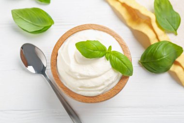 Lezzetli yoğurt kasede, fesleğen ve kaşık beyaz ahşap masada, düz yerde