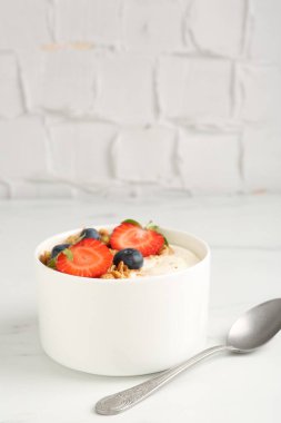 Tahıllı yoğurt, beyaz mermer masada böğürtlen ve kaşık, yakın plan.