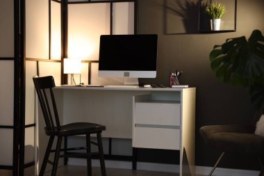 Çalışma masası, bilgisayarı ve kırtasiyesi olan şık bir iş yeri. İç tasarım