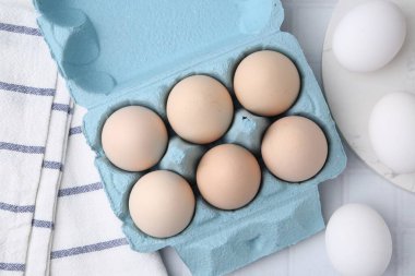 Yumurta kutusunda çiğ tavuk yumurtası, beyaz fayanslı masa, düz.