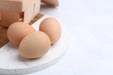 Çiğ tavuk yumurtası ve ahşap yumurta tepsisi beyaz fayanslı masada, yakın plan. Metin için boşluk