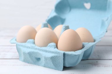 Beyaz ahşap masada yumurta kartonunda çiğ tavuk yumurtası, yakın plan.