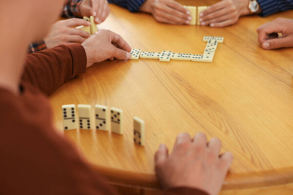 Друзья играют в домино за деревянным столом, крупным планом