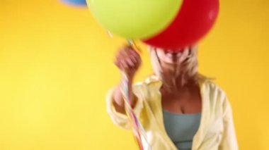 Sarı arka planda renkli balonları olan mutlu bir kadın.