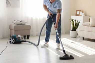 Evin zeminini elektrikli süpürgeyle temizleyen adam, yakın çekim.