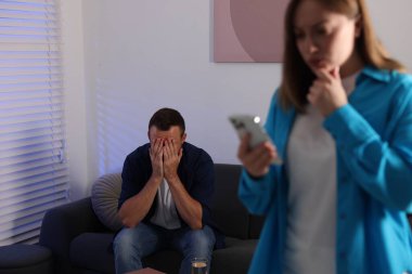 İhanet. Adam elleriyle yüzünü kapatırken karısı evde akıllı telefondan ihanetinin kanıtlarını buluyor.