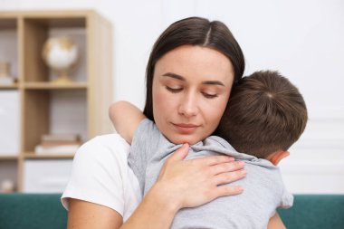 Annesi evdeki kanepede üzgün oğlunu destekleyip kucaklıyor.