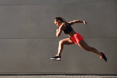 Spor giyimli bir kadın binanın yanında koşuyor, mesaj için yer var.