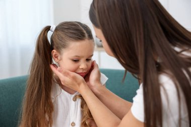 Anne, üzgün kızını evdeki kanepede destekliyor.