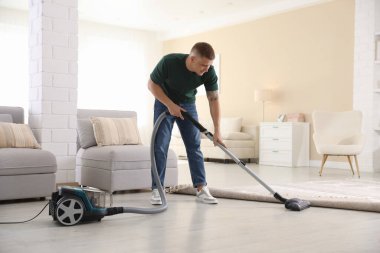 Evin zeminini elektrikli süpürgeyle temizleyen adam.